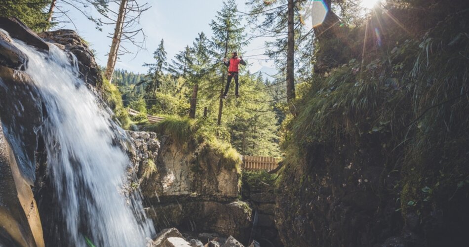 Climber walking on a wire rope, on the left the Häselgehr waterfall.