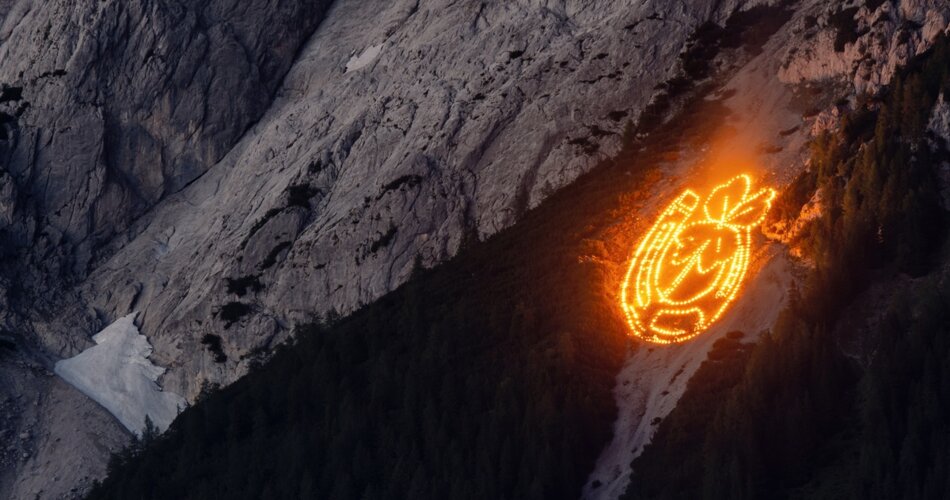 Ein aus kleinen Feuern bestehendes Bild am Berghang. Das Bild zeigt ein Hufeisen und ein sich darin befindendes Kleeblatt. 